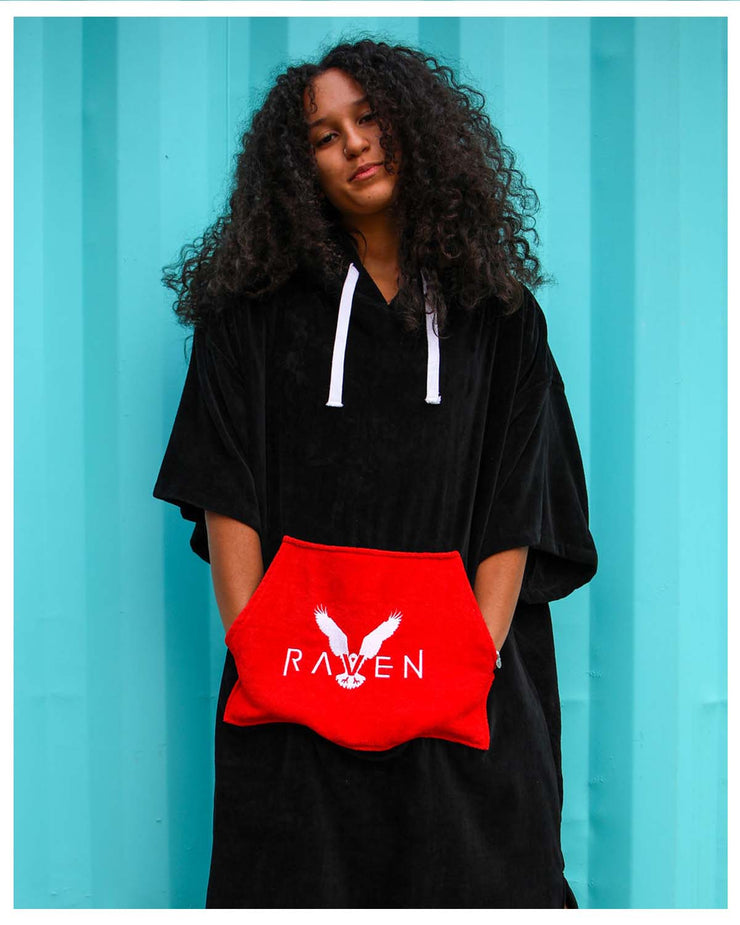 A woman wearing a black hooded towel poncho with a red waistband carrying a towel bag with &
