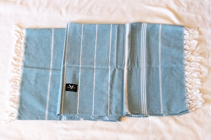 Blue beach towel with white stripes and frayed edges on a white background