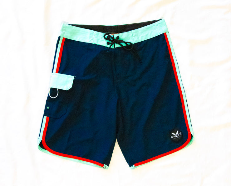 A pair of vintage board shorts in blue with red and white trim, featuring a drawstring waist and a small logo on the left leg.